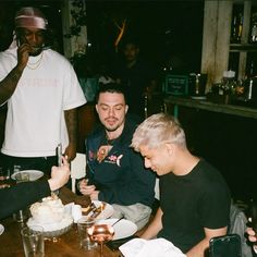 a group of men sitting around a wooden table eating cake and drinking beer at night