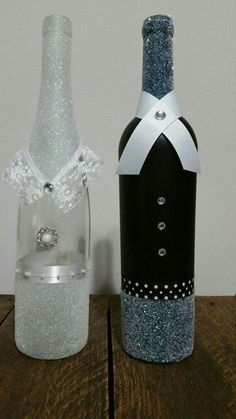 two wine bottles are decorated with silver glitters and white lace, one has a diamond ring on the top