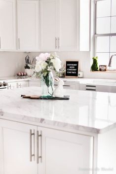 a kitchen with white cabinets and marble counter tops, flowers in a vase on the island