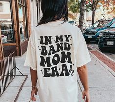 ✦ 🇺🇸SENT TO PRODUCTION AND PRINTED IN THE US🇺🇸 ✦The perfect In My Band Mom Era Graphic TShirt is yours!  ✦ QUICK FACTS ✦ Comfort Colors® C1717 T-Shirt is 100% ringspun cotton (ringspun=comfort) Preshrunk, soft washed, garment-dyed fabric Twill-taped back neck and shoulders ✦ SIZING TIPS ✦ All our garments are UNISEX.  FOR AN OVERSIZED LOOK, SIZE UP 2-3 SIZES For a Relaxed Fit order your Usual Size For a Snug Fit order 1 Size down If you're unsure: Lay your favorite fitting T-Shirt flat and * Band Merch Shirt With Slogan For Concerts, Band Merch Shirt With Slogan, Band Merch Shirt With Slogan For Fans, Band Merch Slogan Shirt For Fans, Cotton Band Merch Tops With Lettering, Marching Band Outfits, Band Shirt Ideas, Marching Band Mom, Marching Band Shirts