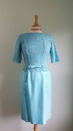 This vintage icy-blue dress is exquisitely tailored, and features an alençon-lace overlay bodice and sleeves; a flattering fitted silhouette with a nipped waist, accented by a darling bow; and a graceful boatneck neckline. Back nylon zip; bodice is lined, skirt unlined of a structured, thick material; pictured on a US size 6/8 dress form. Era: 1960s Label: Sylvia Ann | Includes blue and white ILGWU tag Blue Formal Lace Dress With Lace Bodice, Fitted Light Blue Evening Dress For Formal Occasions, Light Blue Fitted Evening Dress For Formal Occasions, Formal Fitted Light Blue Evening Dress, Elegant Light Blue Lace Dress For Party, Elegant Light Blue Dress With Lace Trim, Fitted Light Blue Mother Of The Bride Evening Dress, Elegant Fitted Light Blue Lace Dress, Vintage Light Blue Dress For Daywear