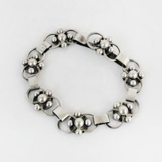 a close up of a bracelet on a white surface with silver balls and metal clasps