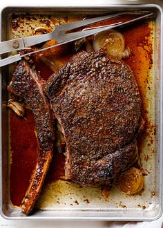 a pan with some meat and vegetables on it next to a pair of tongs