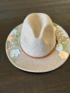 Fedora style hat with textured hand painted flowers.       -Faux leather band with gold buckle detail Material:       -65% Cotton      -35% Polyester Hat measurements:       -2.8" brim      -22.4-23.2" inner circumference      -4.7" height      -Inside circumference is fully ADJUSTABLE - there is a string pull on the inside to adjust to your perfect fit. Care Instructions:      -Spot clean only with damp cloth      -Paint can get wet and will not come off      -Do not put through the washer/drye Spring Festival Flat Brim Felt Hat, Flat Brim Felt Hat For Country Events In Spring, Spring Flat Brim Felt Hat For Country Events, Country Style Felt Hat For Spring, Spring Felt Hat For Country Events With Flat Brim, Country Style Brown Fedora For Spring, Spring Country Style Brown Fedora, Spring Festival Cream Fedora, Adjustable Short Brim Felt Hat For Spring