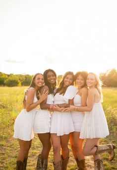 four girls in white dresses and cowboy boots posing for the camera with their arms around each other