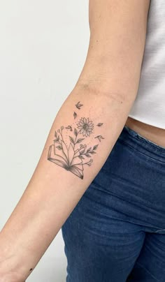 a woman's arm with a book and flowers tattoo on the back of her left arm