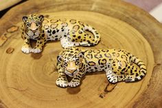 two figurines of leopards sitting on top of a wooden slab with white and black spots