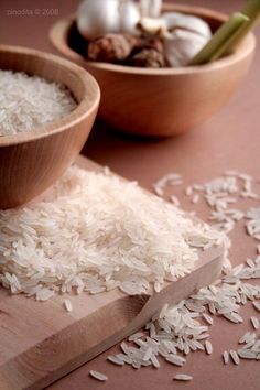 two wooden bowls filled with white rice next to chopsticks and garlic on a table