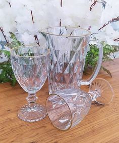 two clear glass vases sitting on top of a wooden table next to white flowers