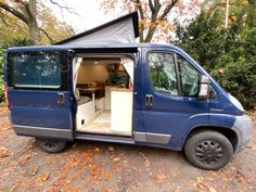 a blue van with its doors open on the road in front of trees and leaves