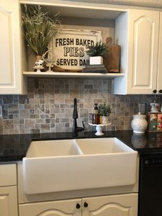 a kitchen with white cabinets and black counter tops is pictured in this image, there are plants on the shelves above the sink