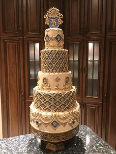 a four tiered wedding cake with blue and gold decorations on the top is sitting on a marble countertop