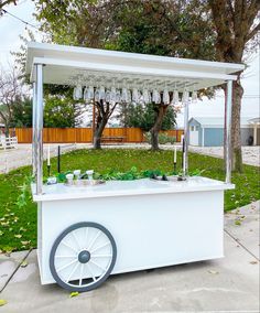 an outdoor ice cream cart with wheels on the sidewalk in front of a tree and grass area