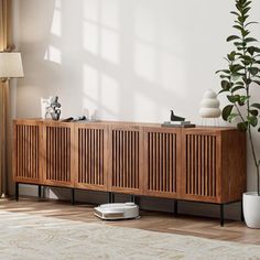 a living room scene with focus on the wooden sideboard and plant in the corner