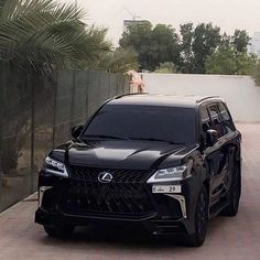 a black car parked on the side of a road next to a tall palm tree