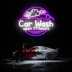 a car wash neon sign with a man washing the car in front of it at night