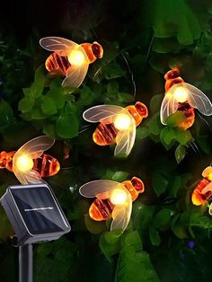 solar powered garden lights with bees on them in the dark, surrounded by green leaves