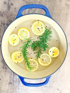 lemons, rosemary and water in a pan on a wooden table with blue handles