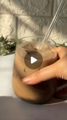 a hand holding a glass with ice cream in it and a straw sticking out of the top