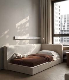 a bed sitting in the middle of a bedroom next to a window with tall buildings behind it