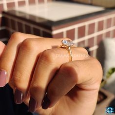 a woman's hand holding a ring with a diamond on it, in front of a brick wall