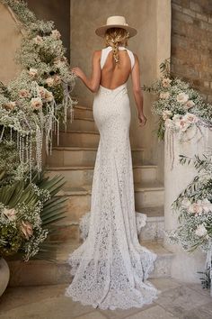 the back of a woman in a white dress and hat standing on steps with flowers