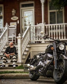 a man sitting on the steps next to his motorcycle in front of a house with stairs