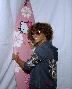 a man holding a pink surfboard in front of a white wall with hello kitty on it