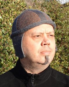 a man wearing a knitted hat looks off into the distance while standing in front of bushes