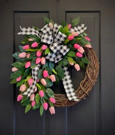 a wreath with pink tulips and green leaves hanging on a black front door