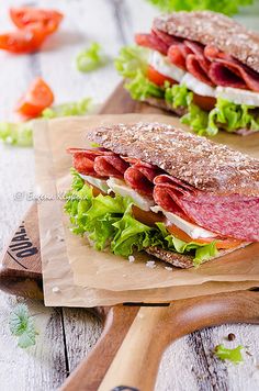 two sandwiches with meat, lettuce and tomato on wooden cutting board next to knife