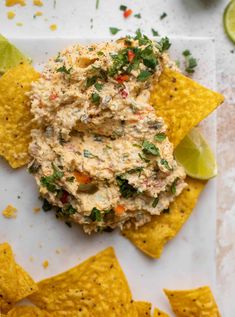 a white plate topped with guacamole and tortilla chips next to lime wedges