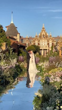 a bride and groom standing in front of a large building with lots of flowers on the ground