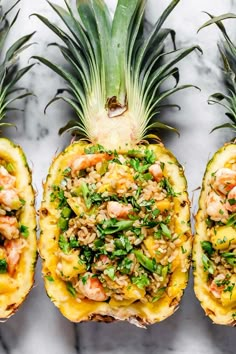 pineapples with shrimp and rice in them on a marble countertop next to two pineapple halves