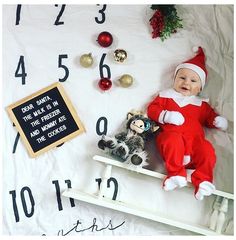 a baby dressed as santa is sitting on a sleigh next to a clock