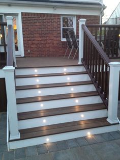 a deck with lights on it and some chairs in the back yard next to a brick building