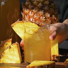 a person is holding a pineapple drink in front of some sliced pineapples