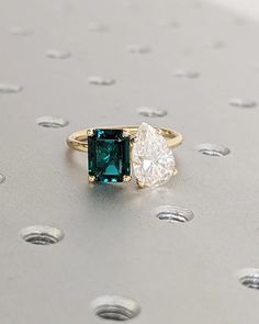 a green and white diamond ring sitting on top of a silver surface with dots around it