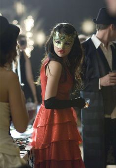 a woman in a red dress and mask standing next to other people at a party