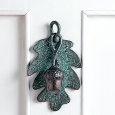 a green metal leaf and acorn hanging on a white door with an oak leaf charm attached to it