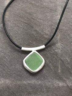 "This individually handcrafted sterling silver pendant features a beautifully smoothed light jade green seaglass nugget. The glass is sourced in Kintyre on the west coast of Scotland.  The naturally tumbled sea glass is set within a fine silver bezel setting, open-backed to allow the light to shine through and enhance the subtle colour of the glass. The pendant is suspended on a sterling silver tube bail on an 16\" black leather lace with sterling silver fittings.  Makes an ideal gift for ladies Green Pendant Jewelry With Adjustable Cord, Minimalist Green Glass Jewelry, Adjustable Green Recycled Glass Necklace, Minimalist Green Jewelry With Recycled Glass, Green Recycled Glass Pendant Jewelry, Green Waxed Cord Necklace For Gifts, Seaglass Necklace, Anniversary Gift For Him, Glass Jewellery