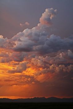 the sky is filled with clouds as the sun sets in the distance over mountains and plains