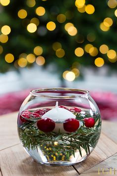 a glass bowl filled with water and candles on top of a wooden table next to a christmas tree