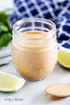 a jar filled with peanut butter next to sliced limes and a spoon on a table