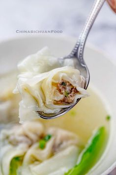 a spoon full of dumplings with meat and vegetables on them, in a white bowl