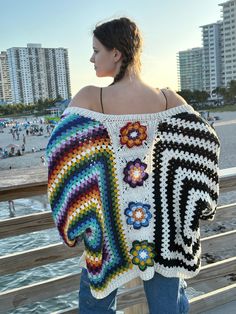 a woman wearing a crocheted sweater standing on a pier next to the ocean