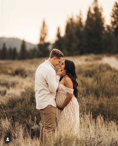 a man and woman standing in tall grass with trees in the backgrouds