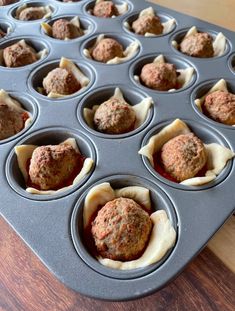 a muffin tin filled with meatballs on top of a wooden table