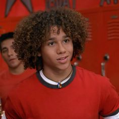 a young man with curly hair wearing a red shirt