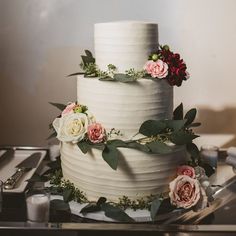 a three tiered cake with flowers and greenery on the top is ready to be cut